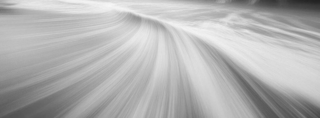 Serene black and white coastal landscape with gentle waves and dramatic clouds at dusk